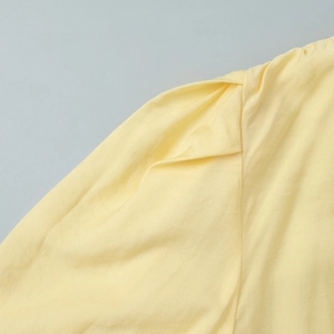 Macro detail of ruffled shoulder stitching and pleat texture on yellow V-neck dress