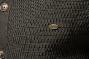 Close-up of olive green knit cardigan with textured resin buttons and metal brand plaque