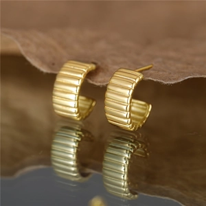 Elegant C-shaped gold-plated silver earrings with horizontal ribbed textures on a leaf