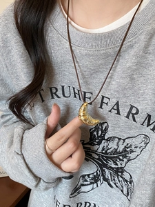 Close-up of golden croissant pendant on a dark leather cord worn with a gray hoodie