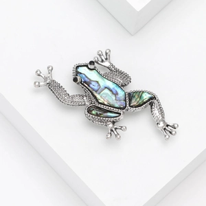 Elegant silver frog brooch featuring iridescent abalone shell inlay on white pedestal