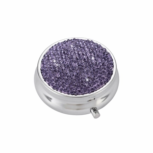 Top view of circular silver pill box with purple rhinestone lid on white background