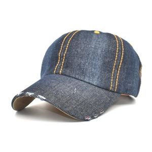 Detail of distressed navy denim baseball cap with yellow contrast stitching and torn brim