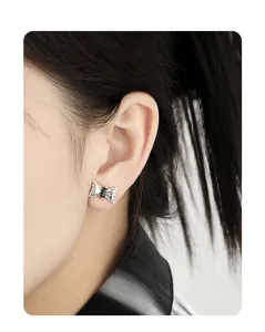 Macro shot of S925 silver bow earring with black zircon on ear, dark style detail