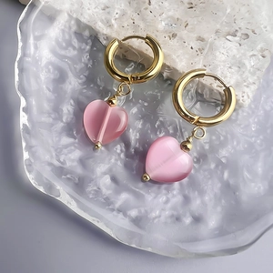 Detail view of 18K gold-plated heart earrings with pink cat-eye stone on artistic tray
