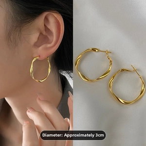 Detail view of 3cm golden twisted hoop earrings on model and white satin background