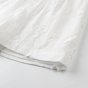 Detailed close-up of white 3D floral embroidery on lightweight cotton summer shirt