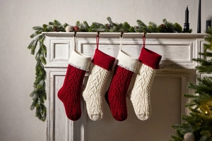 Knitted Christmas stockings with heart tassels hanging on a fireplace for home decor