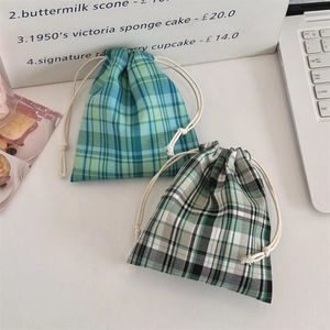 Detail view of cotton drawstring pouches with blue and green plaid patterns on a desk