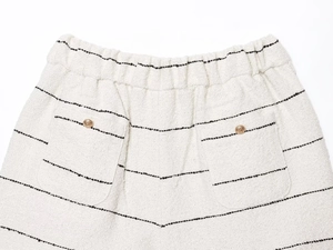 Dettaglio del tessuto in tweed bianco con strisce nere e bottoni dorati incisi sulla tasca