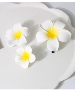 Three realistic frangipani hair clips in different sizes on a white ceramic plate