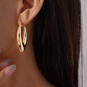 Close-up of a model wearing a hollow teardrop gold hoop earring with a polished metal finish