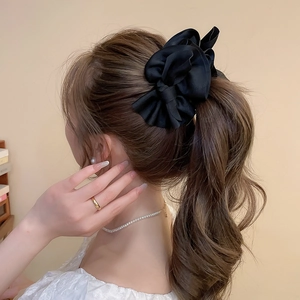 Detail of a large black satin bow hair clip styled on a low ponytail for an elegant look