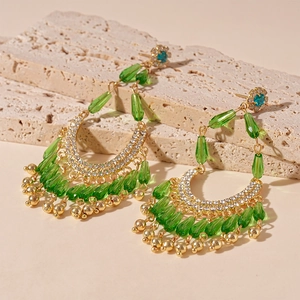 Detailed close-up of Bohemian drop earrings with green crystals on a beige stone base