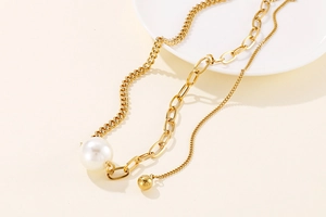 Detail of asymmetric gold necklace featuring a pearl pendant and metal ball charm