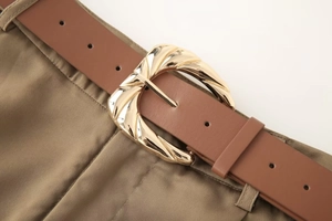 Détail d'une ceinture en cuir marron avec boucle en métal doré sur un pantalon