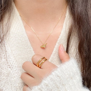 Detail of minimalist gold whale pendant necklace and wavy ring worn on white sweater
