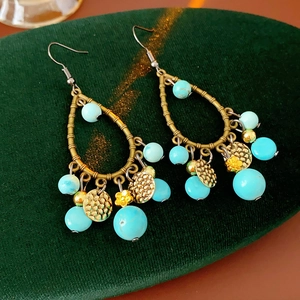 Detailed view of bronze ethnic earrings with turquoise beads on green velvet