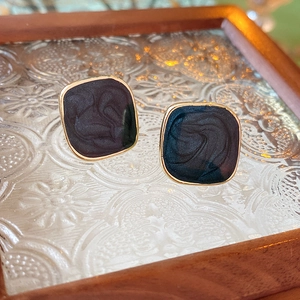 Close-up of gold-edged square stud earrings with dark blue enamel on a glass surface