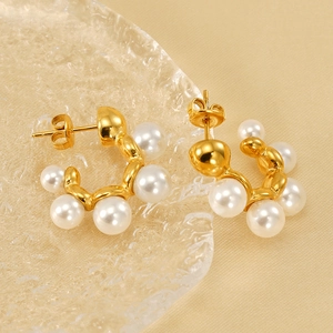 Elegant gold C-shaped pearl earrings on luxury champagne satin and glass background