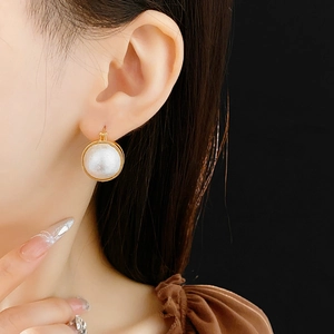 Gros plan d'une boucle d'oreille dorée avec une grande perle blanche sur un modèle