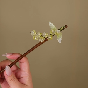 Detailed close-up of dark wood hair stick with delicate yellow-green glass flower buds
