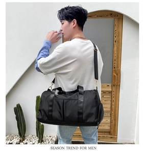 Man carrying a large black nylon sports bag with shoulder strap in a minimalist setting