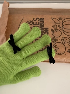 Detail of green knit glove with black bow accents and touchscreen finger design