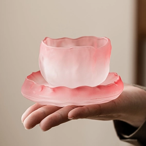 Handheld view of a pink glacier textured glass teacup with a matching scalloped saucer