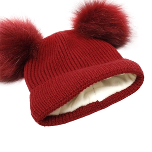 Detail of red knitted winter hat featuring soft double faux fur pom-poms and warm fleece lining