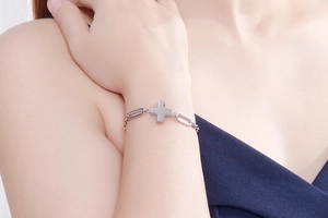 Close-up of a silver paperclip link bracelet with a thick cross charm on a wrist