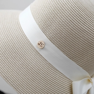 Chapeau de soleil en paille à large bord avec ruban blanc et détail de logo métallique