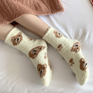 Close-up of thick coral fleece winter socks with cute bear pattern on white bedding