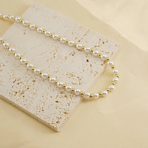 Detail of elegant gold beaded necklace with white pearls on a beige stone block