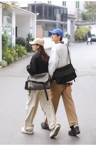 Outdoor shot of black and green canvas messenger bags shown on models walking