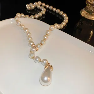 Collier de perles vintage élégant avec pendentif goutte dorée sur plateau blanc