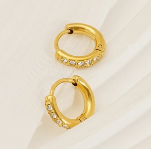 Close-up of gold-plated hoop earrings with clear sparkling gemstones on white fabric