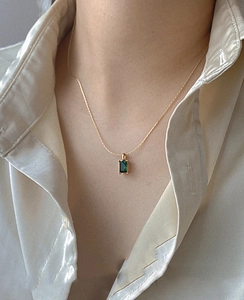 Macro detail of emerald green zircon necklace on silk fabric for vintage luxury look