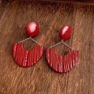 Deep red resin U-shaped earrings with gold chains on vintage wood texture background
