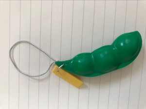 Detalle del juguete antiestrés de soja verde con llavero metálico y etiqueta amarilla
