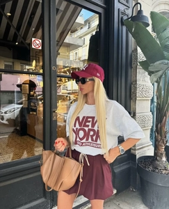 Close-up of a white New York SOHO t-shirt paired with burgundy shorts and a brown bag