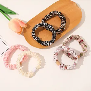 Close-up of 6-piece assorted floral and leopard print satin scrunchies set on a wooden tray