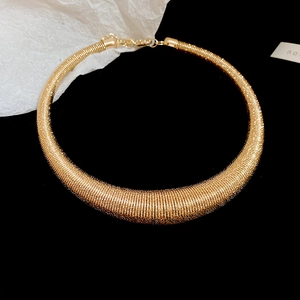 Detailed close-up of a golden metal choker necklace with intricate spiral thread texture