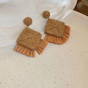 Detail of brown woven straw earrings with tassels on a white ceramic plate