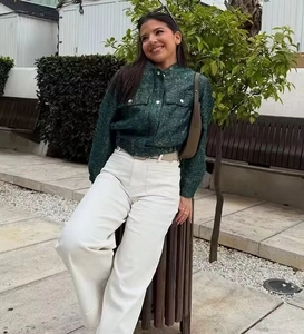 Detail of dark green textured blazer jacket paired with white wide-leg trousers outdoors