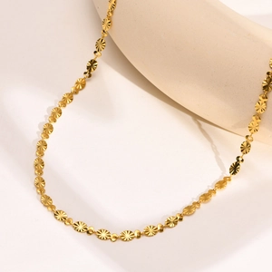 Close-up of golden embossed chain necklace with radial pattern details on beige pottery
