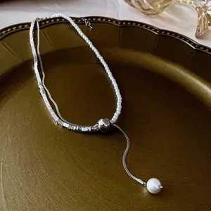 Silver heart tassel necklace with pearls and snake chain on a vintage bronze tray