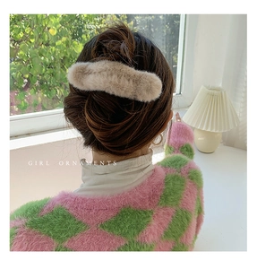 Model wearing a large khaki plush hair claw clip in a cozy natural window light setting