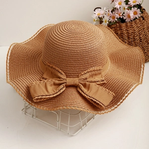Women's summer straw sun hat with elegant wavy brim and large decorative bow detail