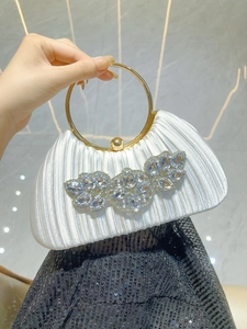 Detailed close-up of white pleated satin evening bag with rhinestone leaf ornament and gold ring handle